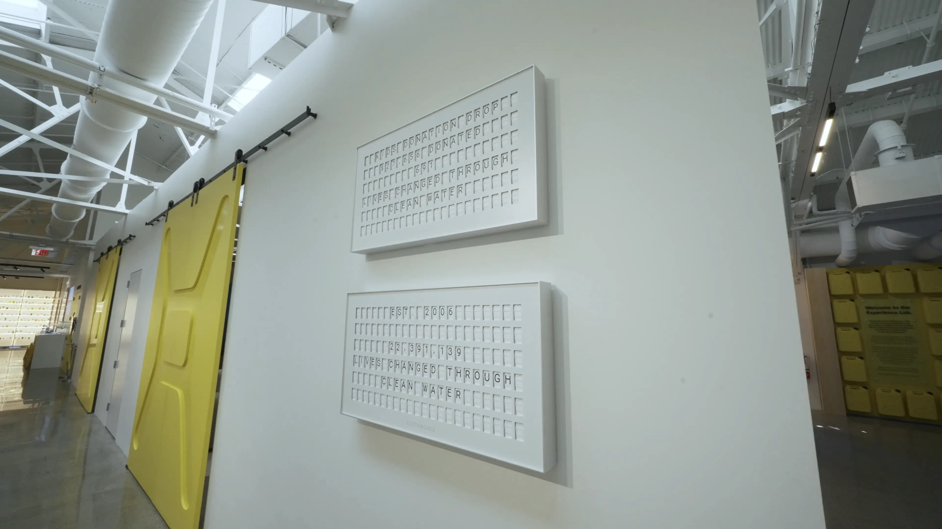 Two white Vestaboards on a wall at charity: water showing lives changed through clean water